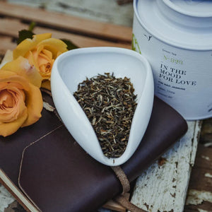 White ceramic dish with tea leaves, yellow roses, and a tea canister on a wooden surface