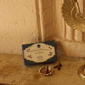Brass incense holder with incense sticks on a wooden surface, next to a box labeled 'Natural Incense Dhoop Cones Brass Holder'.