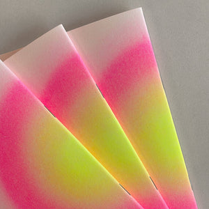 Three overlapping sheets of textured paper with a vibrant pink-to-yellow gradient, displayed on a neutral gray background.