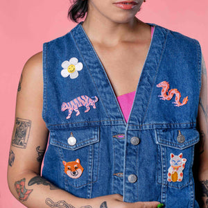 Person wearing a blue denim vest with colorful animal patches on a pink background