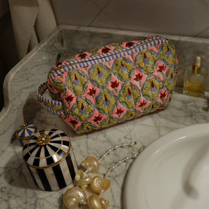 Decorative pouch with floral pattern on a marble surface with jewelry and a bottle.