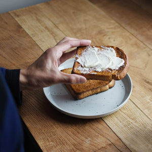 Hand holding a piece of buttered toast over a plate on a wooden table