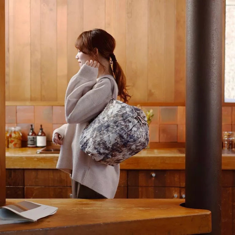Woman holding a floral-patterned bag in a room with wooden walls and a counter.