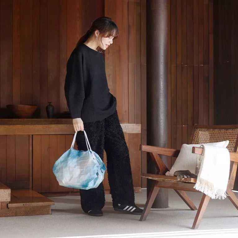 Person holding a blue patterned bag in a room with wooden furniture and a chair.