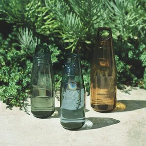 Three transparent water bottles with different designs on a stone surface with greenery in the background