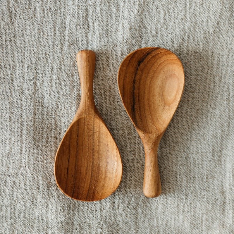 Two wooden spoons on a textured fabric surface, one spoon is empty and the other is holding small dried flowers.