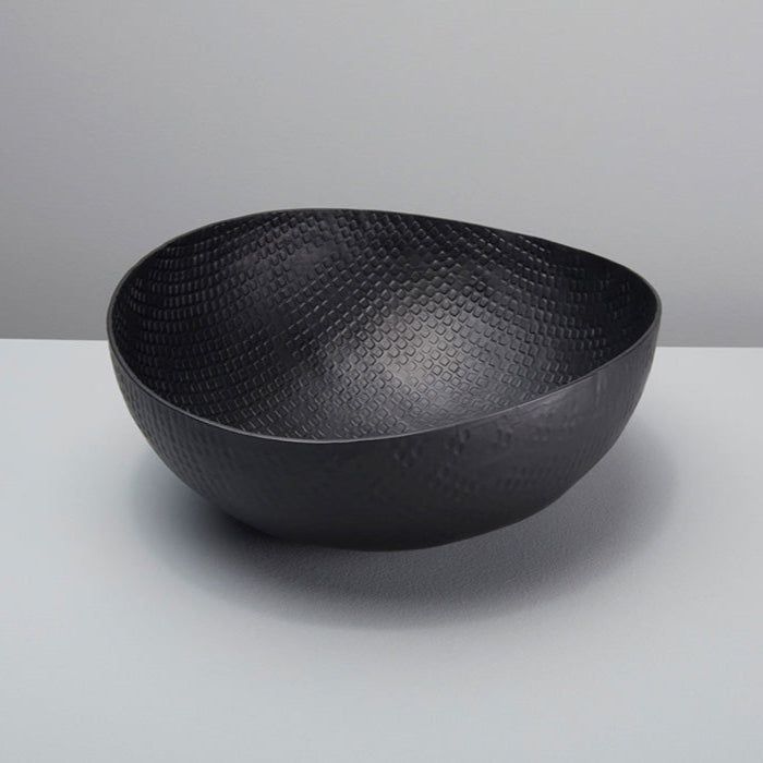 A black aluminum bowl with a textured crosshatch pattern, placed on a white surface against a plain background.