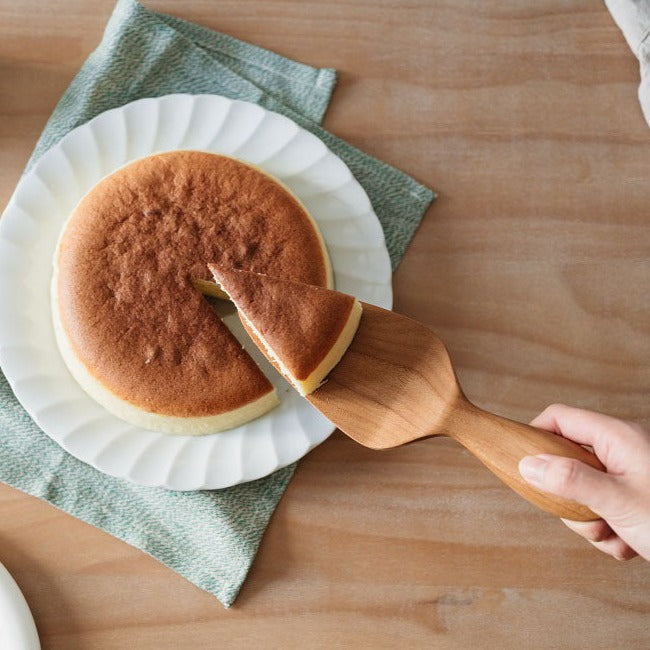 A cake being served using a wooden cake server, with a focus on the server tool.