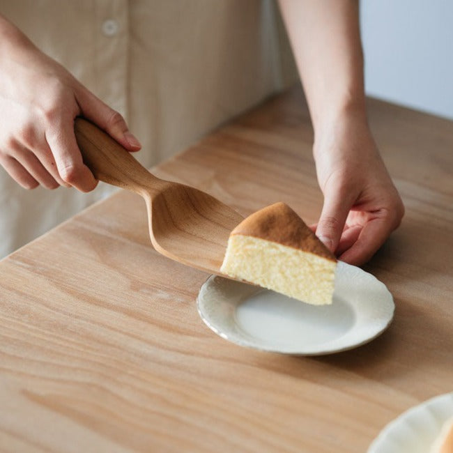 A cake being served using a wooden cake server, with a focus on the server tool.