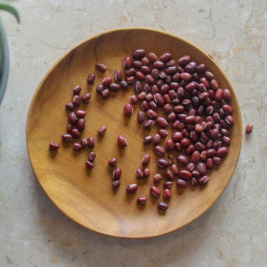A wooden dessert plate with teak wood grain, containing some dried fruit pieces.
