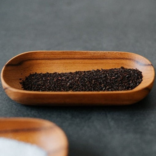 A rectangular Teak Wood Saucer filled with black sesame seeds, placed on a dark surface.