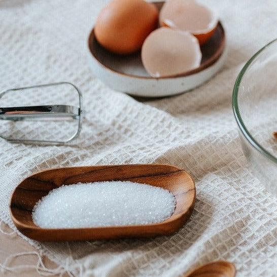 A rectangular Teak Wood Saucer filled with black sesame seeds, placed on a dark surface.